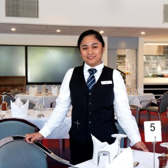 Student Marion stands at Bentley Pines Training Restaurant, she's wearing a suit jacket and a tie.