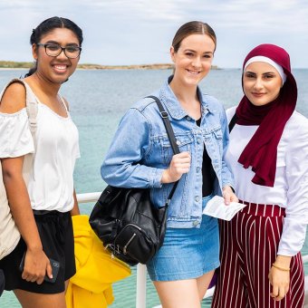 Five students standing on a boat. An island is in the background