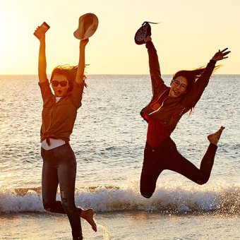 Students jumping in water at the beach, at sunset