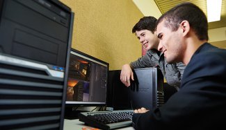 Two people in front of a computer displaying a computerized game