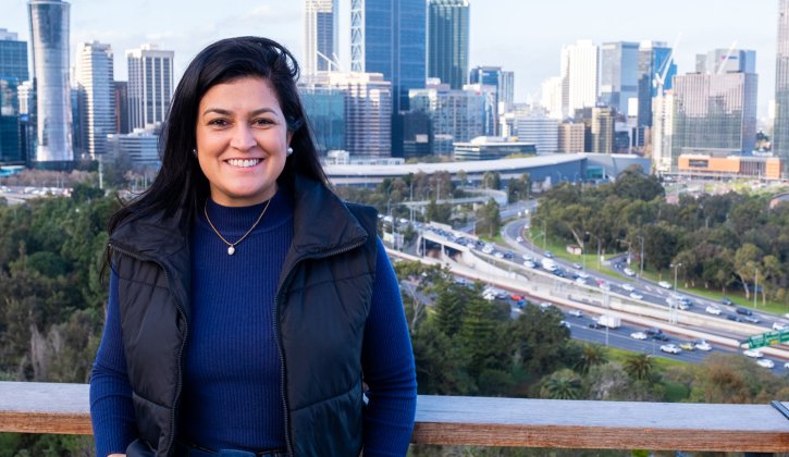 Student stands towards the camera smiling, in the background is a scenic view of the Perth city skyline.