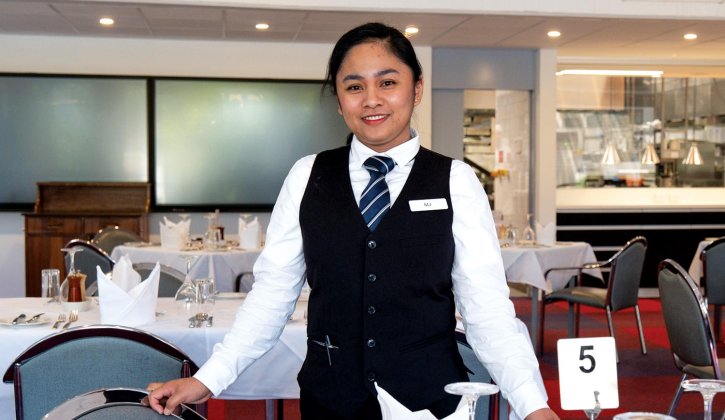 Student Marion stands at Bentley Pines Training Restaurant, she's wearing a suit jacket and a tie.