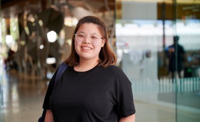 Student Athena standing in foyer of Perth TAFE campus. She wears a black t-shirt and a backpack on one shoulder. She faces towards the camera with a big smile.