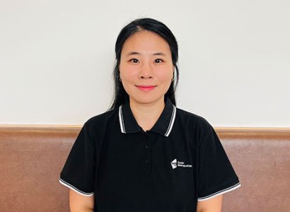 Jinjoo Park sites on a light pink long seat. She is positioned in the centre of the image. She's wearing a black polo shirt with &quot;South Metropolitan TAFE&quot; written on the right of the shirt. She's smiling and looking into the camera. She has brown hair that's pulled back. She has brown eyes.