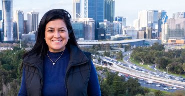 Student Juliana faces towards the camera smiling. In the background is an impressive view of the Perth skyline.